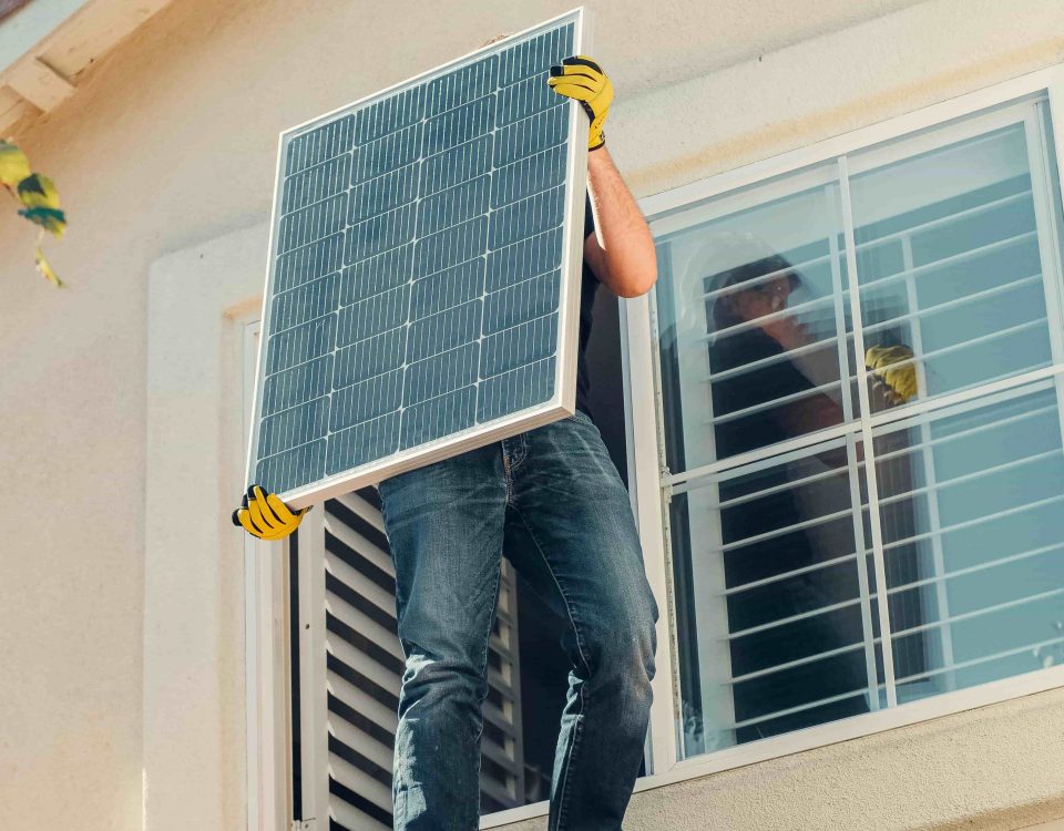 Ein Mann steht auf einem Dach um eine Photovoltaikanlage zu installieren. Das Bild wirkt fröhlich und voller Vorfreude auf die Zukunft.