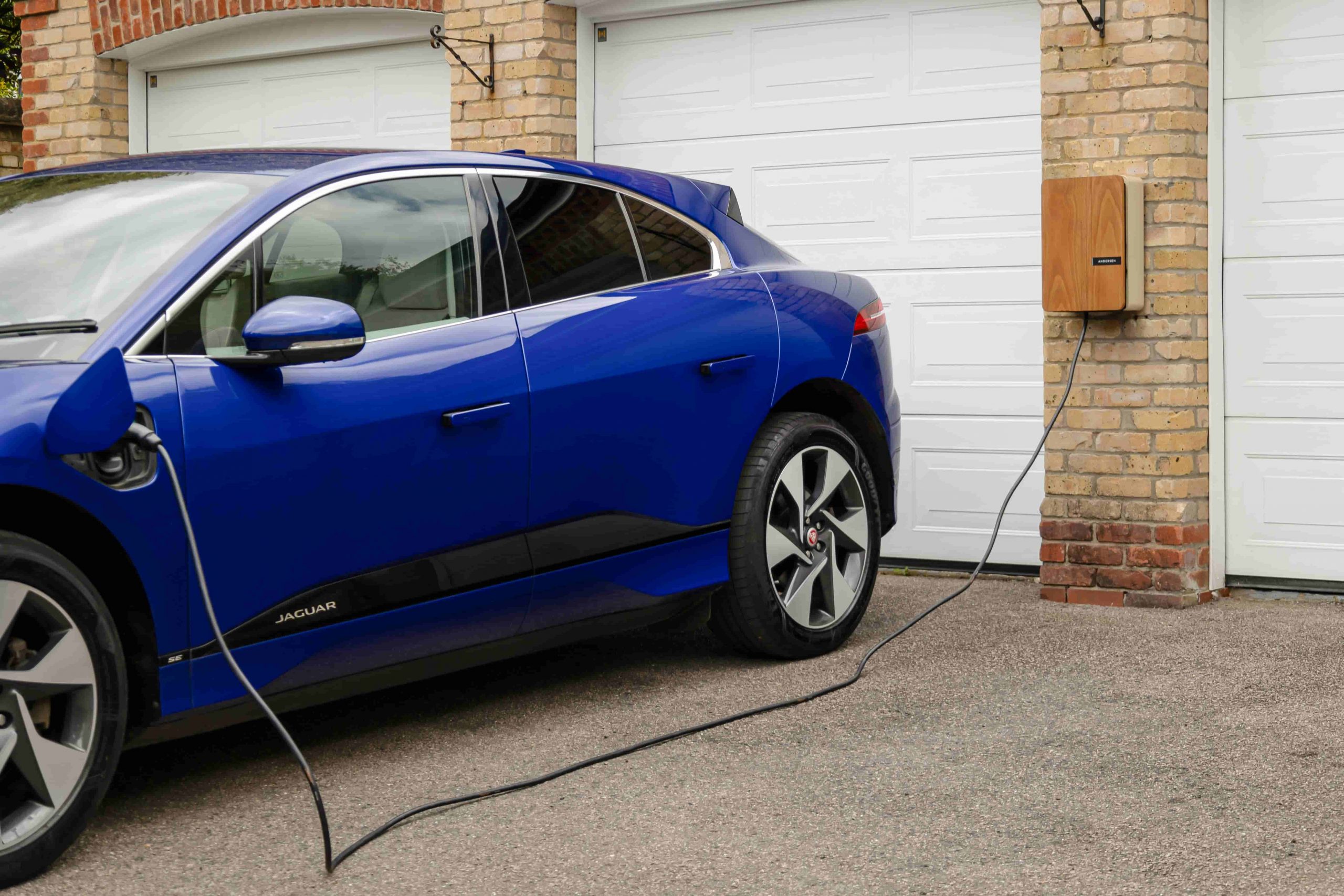 Ein Elektrofahrzeug läd mithilfe einer Wallbox an vor der Garage eines Hauses und veranschaulicht eine intelligente Energieoptimierung